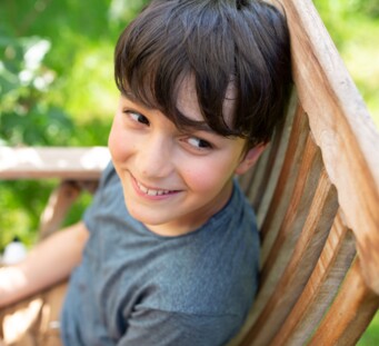 Junge sitzt draußen auf einer Bank und lächelt